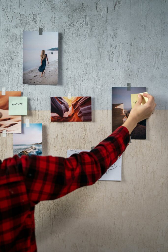 Hand placing sticky notes on a moodboard with travel and nature photos.