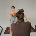 A creative studio photoshoot featuring a model with flowers and a photographer at work.
