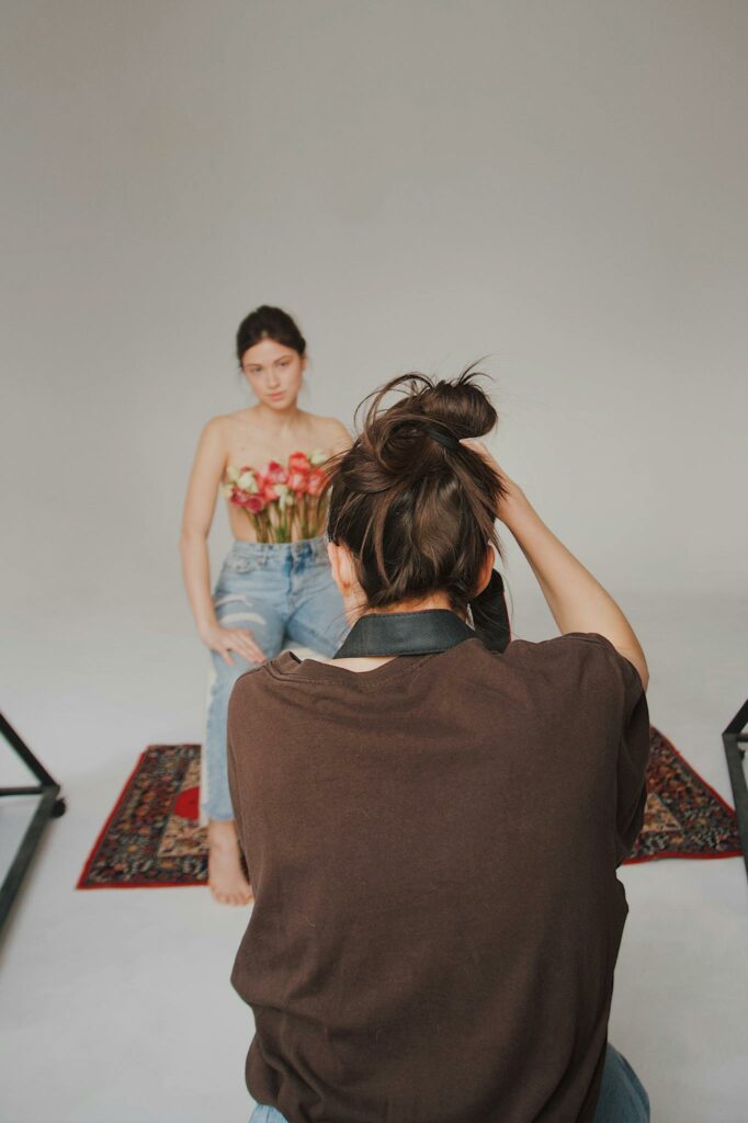 A creative studio photoshoot featuring a model with flowers and a photographer at work.